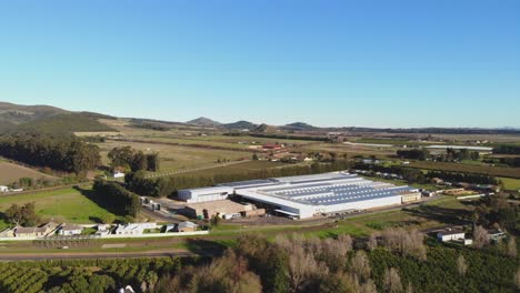 Drone-footage-captures-a-factory-from-an-aerial-side-view,-showcasing-the-harmonious-blend-of-industrial-infrastructure-with-the-natural-beauty-of-rolling-hills-and-lush-greenery