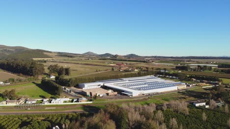 drone footage captures a factory from an aerial side view, showcasing the harmonious blend of industrial infrastructure with the natural beauty of rolling hills and lush greenery