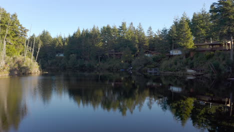 pristine river with reflection of beautiful houses surrounded by coniferous tree at fahys lake in bandon, oregon