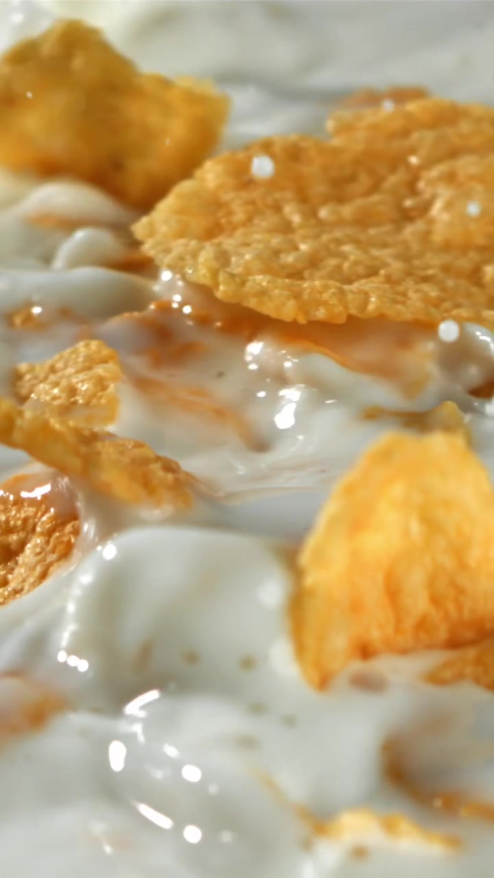Cornflakes dorati che schizzano nel latte bianco fresco al rallentatore