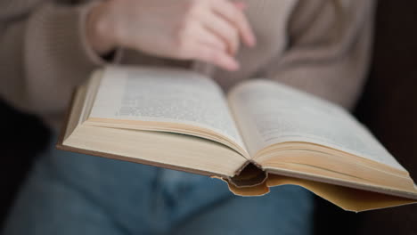 partial view of woman hand gently flipping through a book, showcasing the tactile interaction with pages in soft focus, with text on the pages visible