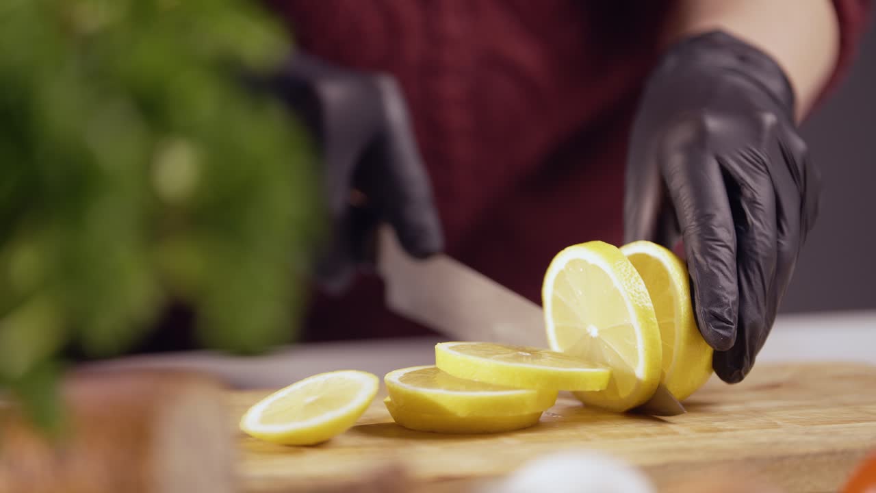 Slow-motion close-up of a chef slicing a fresh lemon on a wooden board. The sharp knife glides smoothly, revealing juicy texture. Black gloves ensure hygiene, with tomatoes and herbs in the background