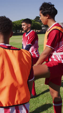 video vertical de un grupo diverso de fútbol masculino en el campo de estiramiento