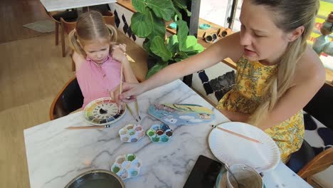 mother and daughter painting pottery in cafe