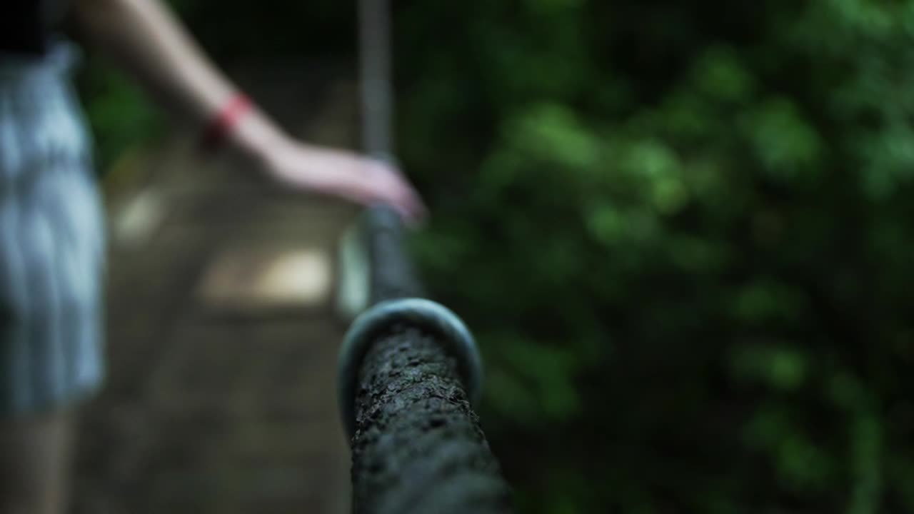 Lady's hand holding on to a rope of a hanging rope bridge as she crosses