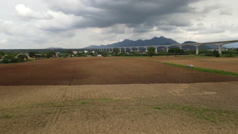 4k aerial dolly out shot capturing the large piece of newly tilled agriculture farmland with muak lek mountains in the background and high-speed train line across the frame