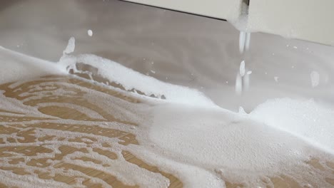 close up of foam from a dishwasher leaking on a wooden floor