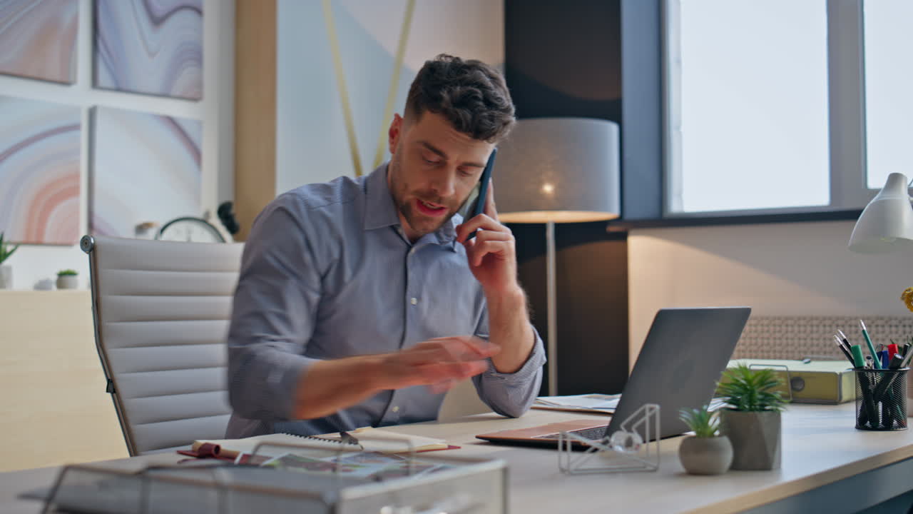 Travl medarbejder taler i mobiltelefon og arbejder på pc på kontoret tæt på. Direktør taster på bærbar computer.