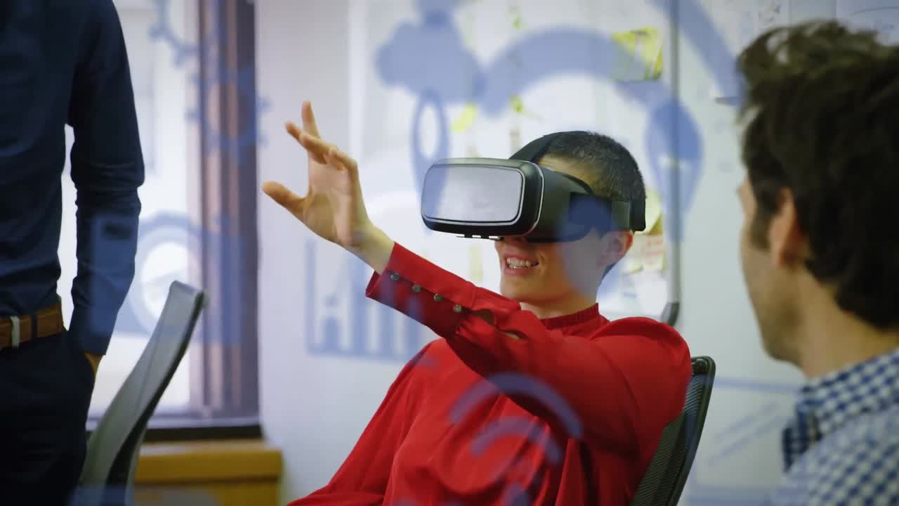 múltiples iconos digitales azules flotando contra una mujer de negocios caucásica que usa auriculares vr en la oficina