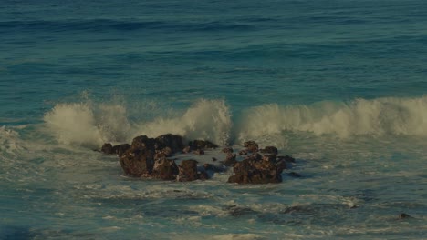 the camera follows the white capped crest of the aqua waters of the pacific ocean as the crash into shore on the volcanic beach in hawaii on the island of oahu