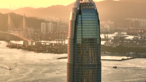 aerial orbiting shot of ifc international finance centre in front of industrial harbor during golden hour - drone establishing shot - hong kong city metropolis, asia