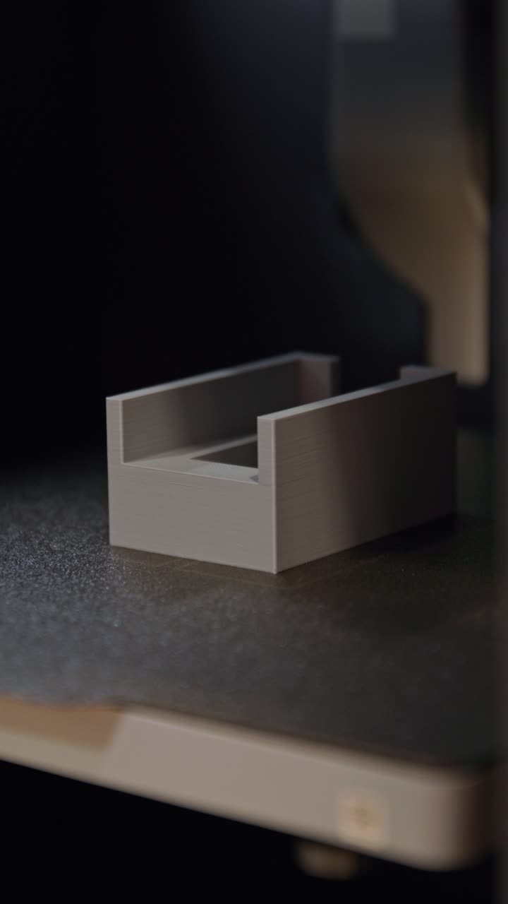 Inquadratura verticale ravvicinata di una mano che rimuove con cura un prototipo in plastica appena stampato in 3D da una superficie di lavoro