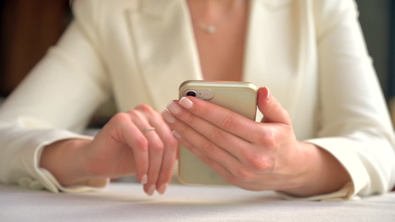 Woman in a white blazer scrolling on her phone at a table at a restaurant