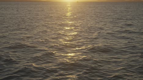 gentle waves in motion during sunset, dark blue water, and orange sun reflection