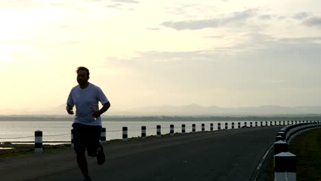 men use a smartphone to listen to music and running in the time during sunrise on dam road exercise. living healthy lifestyle concept.