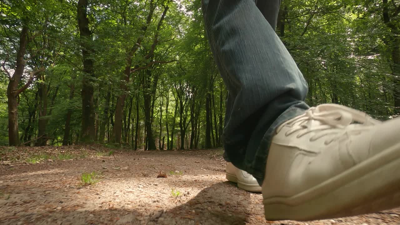 Closeup shot of a men steps in blue jeans and white shoes on a forest path