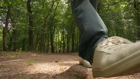 primer plano de un hombre caminando con jeans azules y zapatos blancos en un sendero forestal