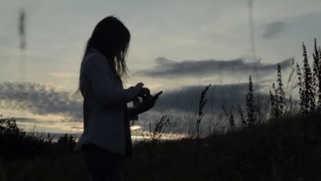 Woman--using-a-cellphone-in-sunset-landscape