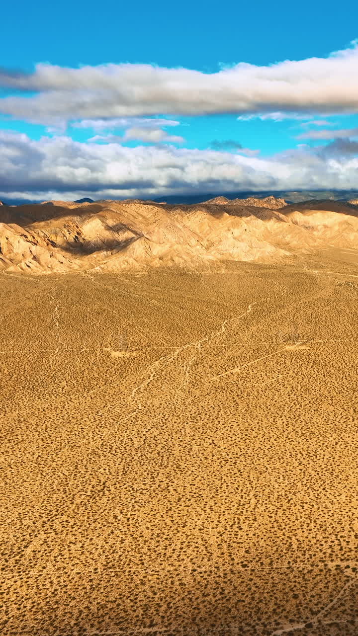 Plain deserted landscape surrounded by rocks. Beautiful blue sky with white clouds contrasting with yellow scenery of the desert. Top view. Vertical video
