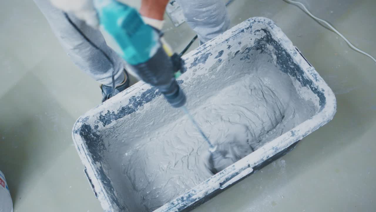 Mixing Construction Material in a Bucket: A Close-Up View of a Worker Using a Drill to Blend Concrete Mixture for a Building Project