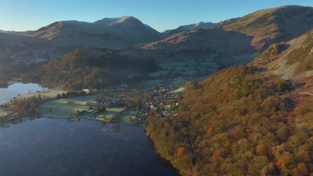 pueblo junto al lago rodeado de montañas y bosques al amanecer en otoño con vuelo lateral hacia la ladera boscosa