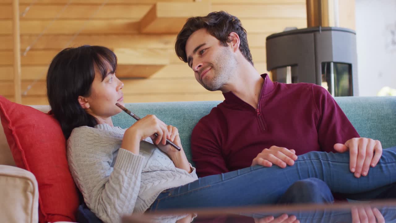 video de la vista de atrás de una feliz pareja diversa sentada en el sofá con un teléfono inteligente