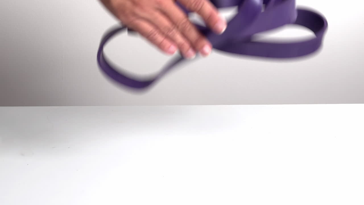 Hand Drops and Picks Up a Purple Resistance Band on White Background