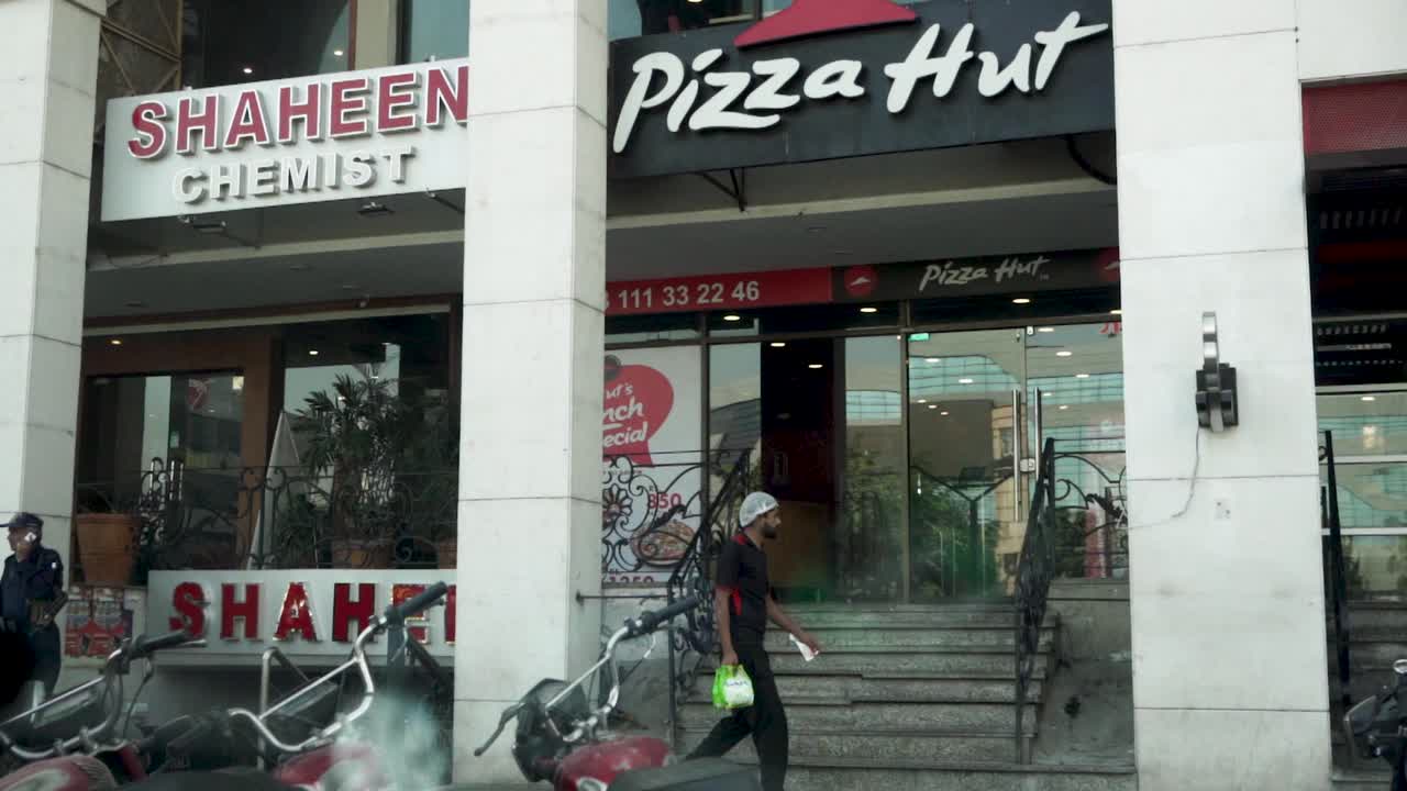 Experience the tantalizing charm of a Pizza Hut from a captivating slow-motion close-up, showcasing a welcoming shopkeeper stepping outside to greet you.