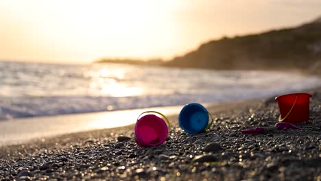 Juguetes-Para-Niños-En-Una-Playa-Con-Olas-En-El-Fondo-Durante-La-Puesta-De-Sol