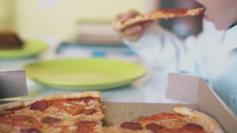 el niño come pizza sabrosa de una caja de cartón en la mesa en cámara lenta