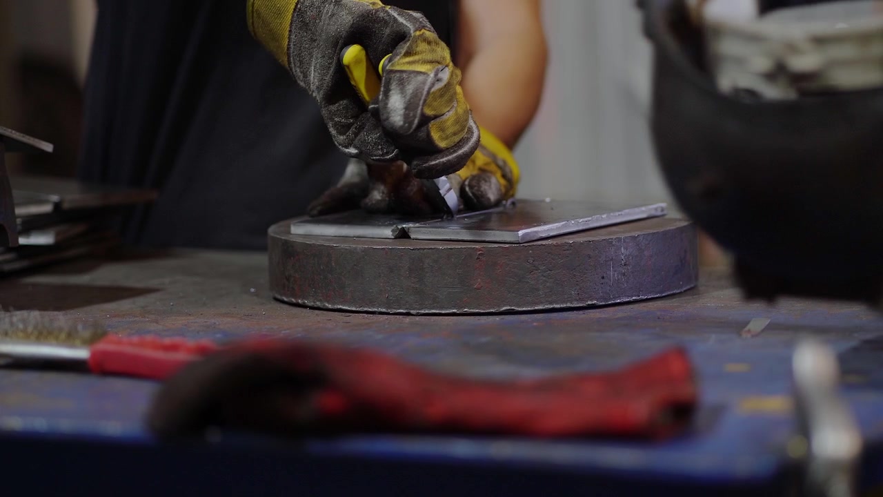 Closeup of a worker's hands using pliers on a metal plate after welding.