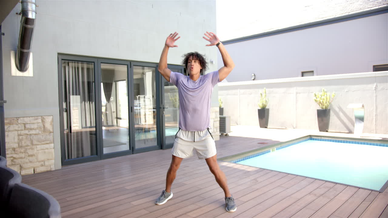 Exercising outdoors, man jumping on wooden deck near swimming pool