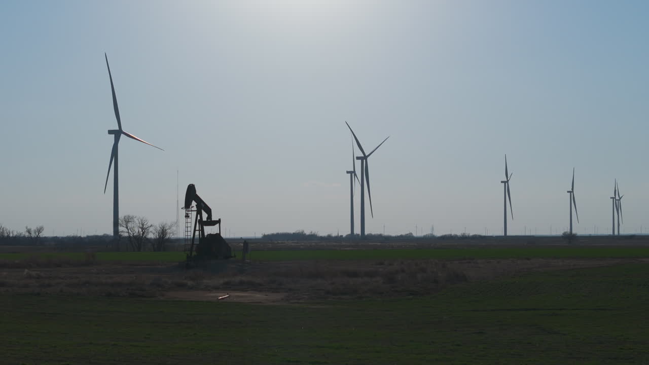 oklahoma - silueta de bomba de petróleo con una fila de turbinas eólicas en el fondo