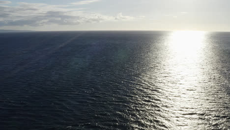 aerial dolly out to sea as sunlight ray bounces on ocean surface with ripples and current