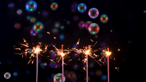 las chispas arden y brillan contra un fondo negro con burbujas de jabón de arco iris voladoras. los fuegos artificiales se encienden en la fiesta, el papel tapiz de año nuevo o navidad con luces y burbuja de jabón. cámara lenta. cerrar