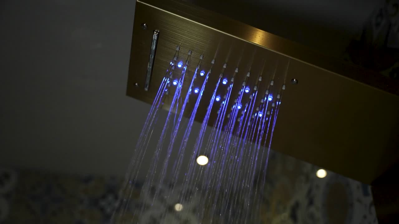 Modern rainfall shower head with blue LED lights spraying water inside a tiled bathroom