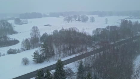 aerial view flying over a countryside road, during blizzard on a gloomy winter day