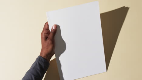 video of hand of african american man holding book with blank pages, copy space on yellow background