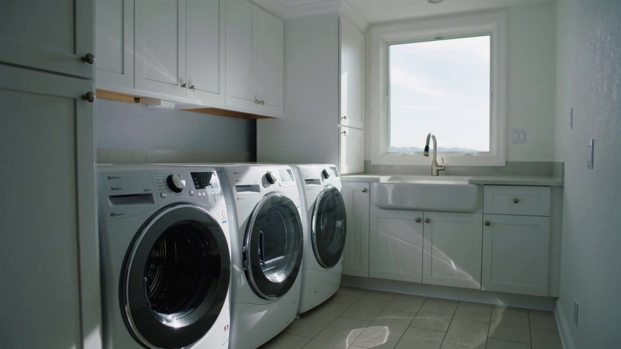 Shifting sunlight through window casting sheen across three frontload machines in home laundry room