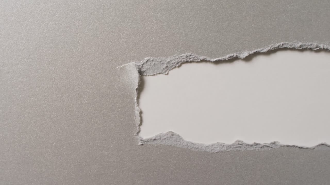 Video of close up of torn grey paper on white background
