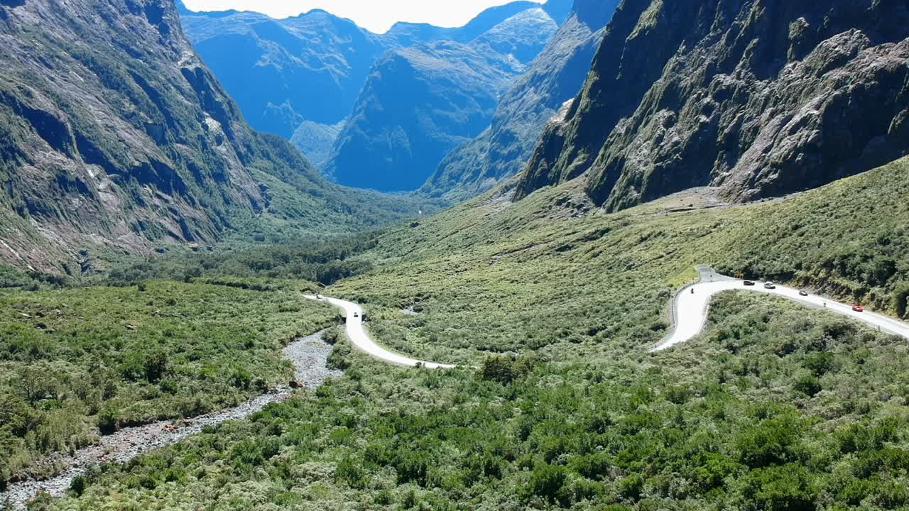 toma aérea de un valle en el parque nacional de fiordland con autos conduciendo en un camino sinuoso en un día soleado