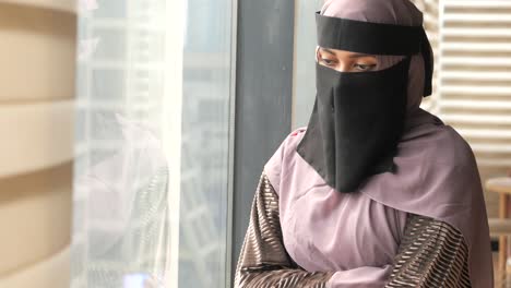 pensive muslim woman in niqab looking out window