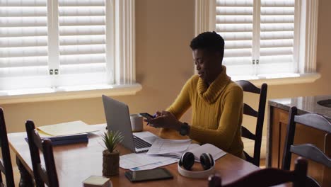 Afroamerikanische-Frau,-Die-Während-Der-Arbeit-Von-Zu-Hause-Aus-Auf-Dem-Smartphone-Spricht-Und-Einen-Laptop-Benutzt