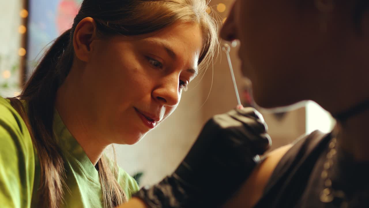 Female Tattoo Artist Speaking with Client as Doing Tattoo on Upper Arm