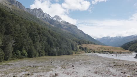 Wide-view-of-a-valley-with-a-river,-forests-and-mountains-on-a-sunny-summer-day-in-Rees-Dart-track,-New-Zealand