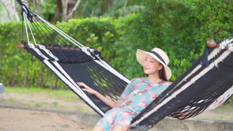 young barefoot asian woman with large hat swings on hammock