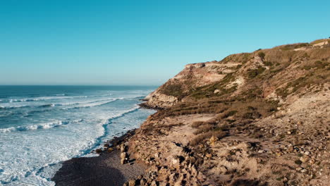 Imágenes-Panorámicas-De-Drones-Revelan-Una-Colina-Costera,-Con-Olas-Acariciando-Su-Costado