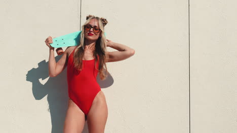 mujer elegante en un traje de baño rojo posando con una patineta