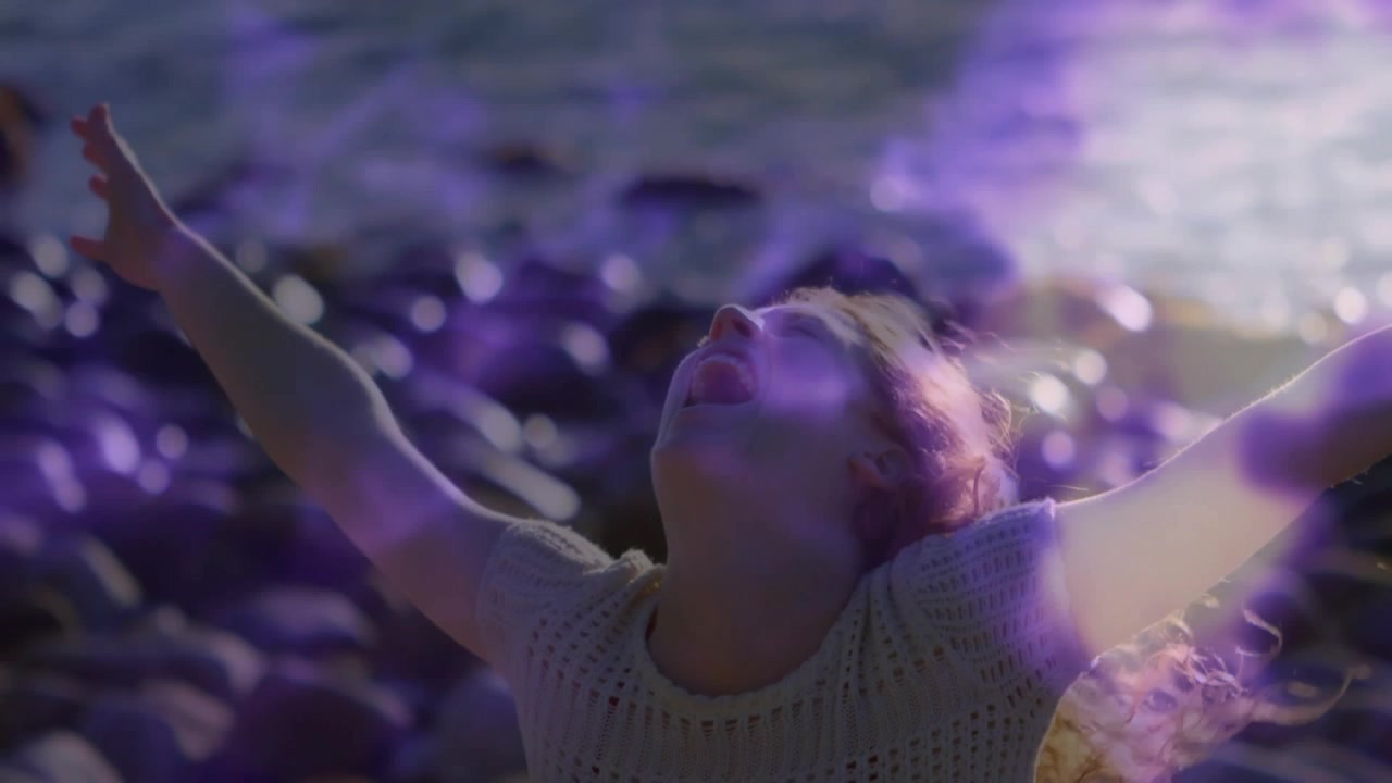 Woman raising arms invoking swirling purple energy on rocky shoreline for technology demo
