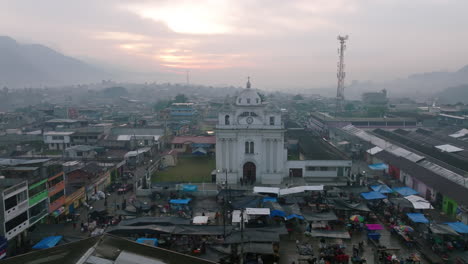 Slow-aerial-flyover-and-rotation-around-the-central-square-in-San-Juan-Ostuncalco,-showing-the-market-and-the-cathedral-in-the-background